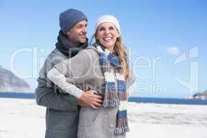 Smiling couple standing on the beach in warm clothing