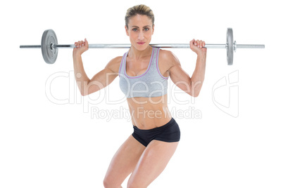 Strong female crossfitter lifting barbell behind head looking at
