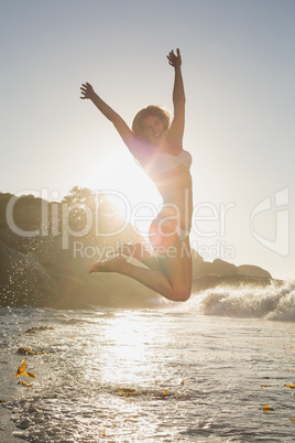 Beautiful jumping blonde in white bikini at the beach