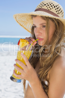 Pretty smiling blonde in bikini sipping cocktail on the beach