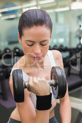 Fit smiling brunette lifting heavy black dumbbell