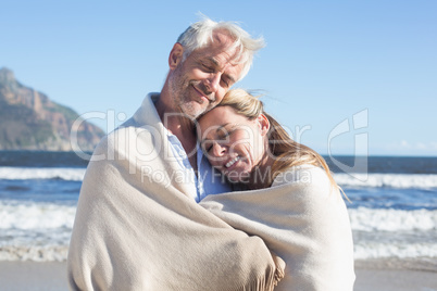 Smiling couple wrapped up in blanket on the beach