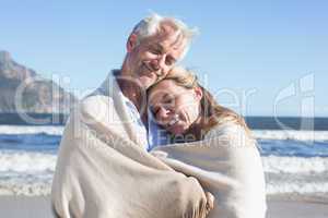 Smiling couple wrapped up in blanket on the beach