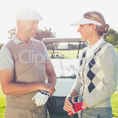 Happy golfing couple chatting with golf buggy behind