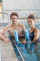 Man and woman standing with foam rollers in the pool