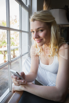 Pretty blonde sitting by the window sending a text