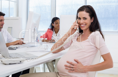 Casual pregnant businesswoman talking on phone at her desk