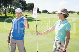 Lady golfer holding eighteenth hole flag for cheering partner