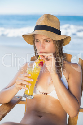 Pretty blonde relaxing in deck chair on the beach with cocktail