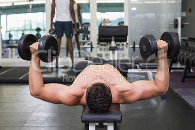 Shirtless bodybuilder lying on bench lifting heavy dumbbells