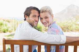 Cute couple sitting on bench together smiling at camera