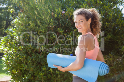 Fit woman holding exercise mat in the park