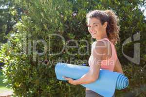 Fit woman holding exercise mat in the park