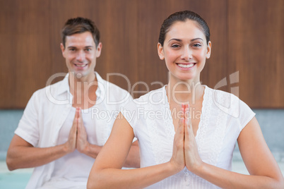Smiling couple in white sitting in lotus pose with hands togethe