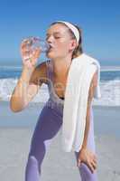 Sporty tired blonde drinking water on the beach