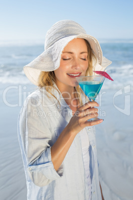 Smiling blonde relaxing by the sea sipping cocktail