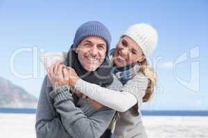 Attractive couple hugging and smiling at camera on the beach in