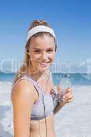 Sporty blonde on the beach smiling at camera with water bottle