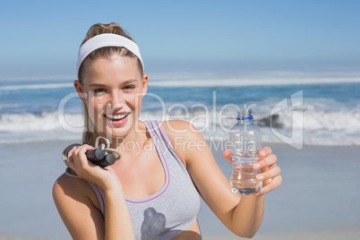 Sporty happy blonde standing on the beach with bottle and skippi