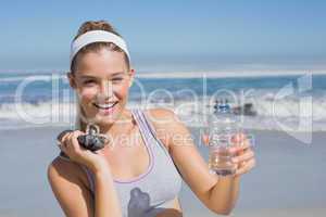 Sporty happy blonde standing on the beach with bottle and skippi