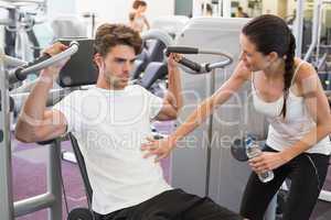 Fit man using weights machine for arms with his trainer