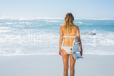 Blonde surfer in white bikini holding her board on the beach