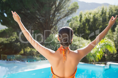 Brunette in sarong standing with arms out by the pool