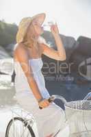 Beautiful blonde in white sundress on bike drinking water at the
