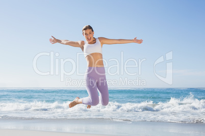 Sporty blonde jumping on the beach with arms out