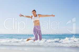 Sporty blonde jumping on the beach with arms out