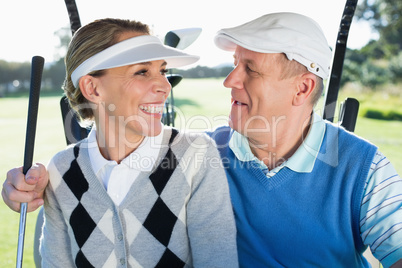 Happy golfing couple sitting in golf buggy smiling at each other