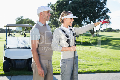 Happy golfing couple looking at course with golf buggy behind