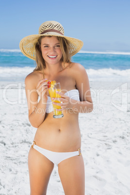 Pretty smiling blonde in bikini sipping cocktail on the beach