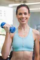 Fit brunette lifting blue dumbbell listening to music