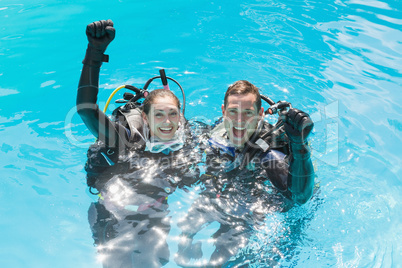 Smiling couple on scuba training in swimming pool looking at cam