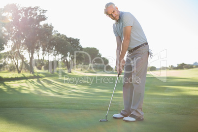 Handsome golfer putting ball on the green