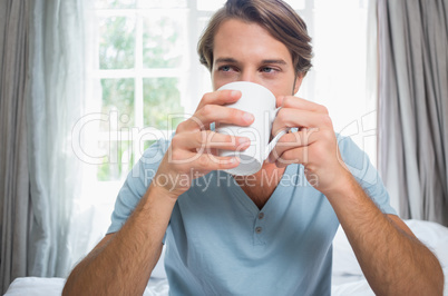 Handsome man sitting on bed drinking coffee