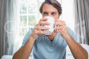 Handsome man sitting on bed drinking coffee