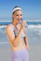 Sporty happy blonde drinking water on the beach