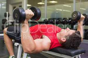 Bodybuilder lying on bench lifting dumbbells