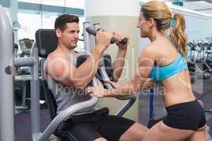 Personal trainer coaching bodybuilder using weight machine