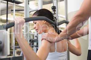 Fit brunette using weights machine for arms with trainer touchin