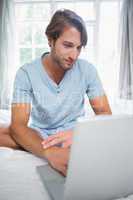 Handsome smiling man sitting on bed using laptop