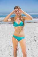 Fit smiling woman in bikini on the beach making heart shape with