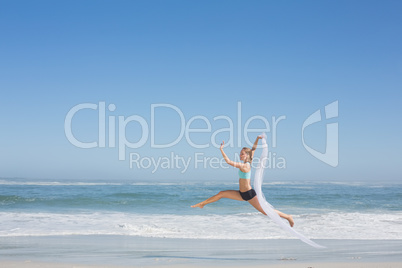 Fit woman jumping gracefully on the beach with scarf