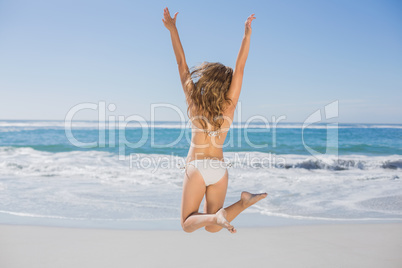 Fit woman in white bikini leaping on beach