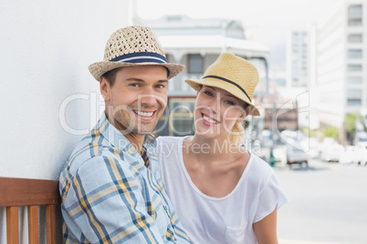 Young hip couple sitting on bench smiling at camera