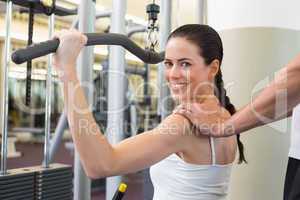 Fit brunette using weights machine for arms with trainer touchin