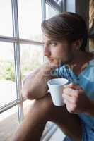 Thoughtful man sitting by the window having coffee