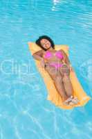Smiling woman in pink bikini lying on lilo in swimming pool